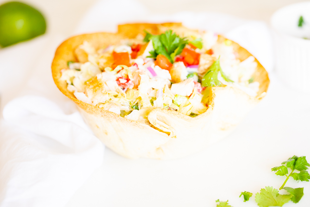 A chicken taco salad in a homemade tortilla bowl on a white plate.