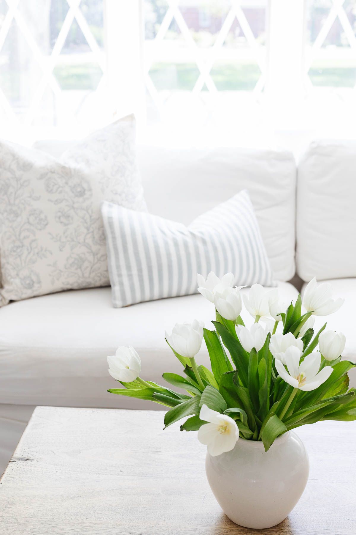 white tulips in a flower vase on a coffee table in a white living room.