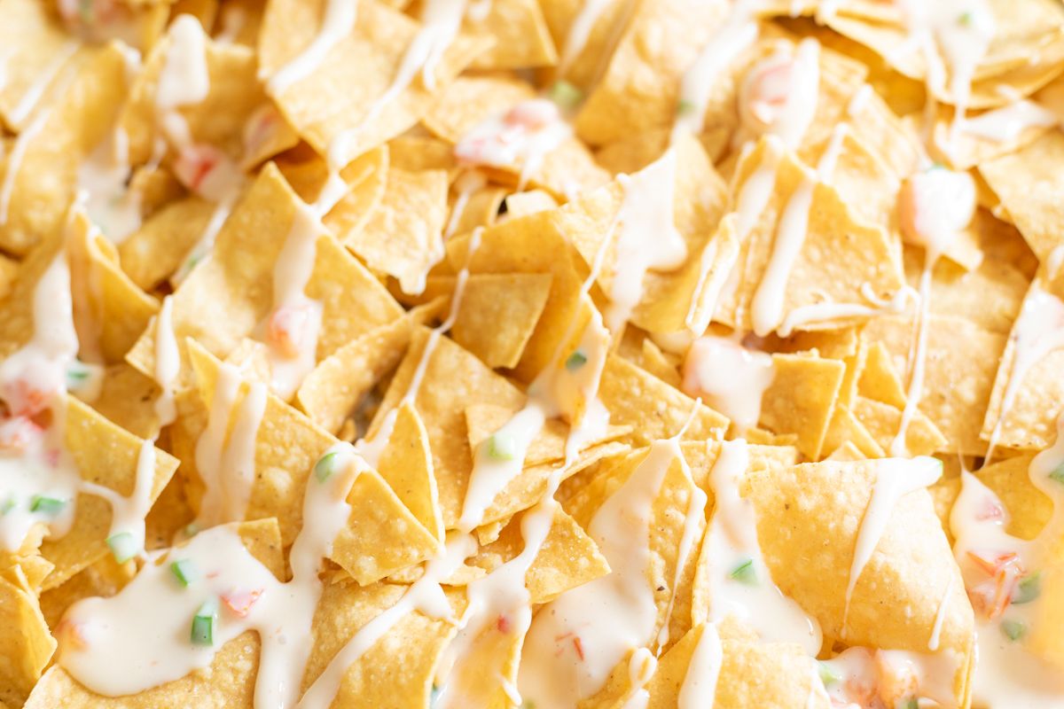 A sheet pan with tortilla chips covered in queso for a chicken nacho recipe.