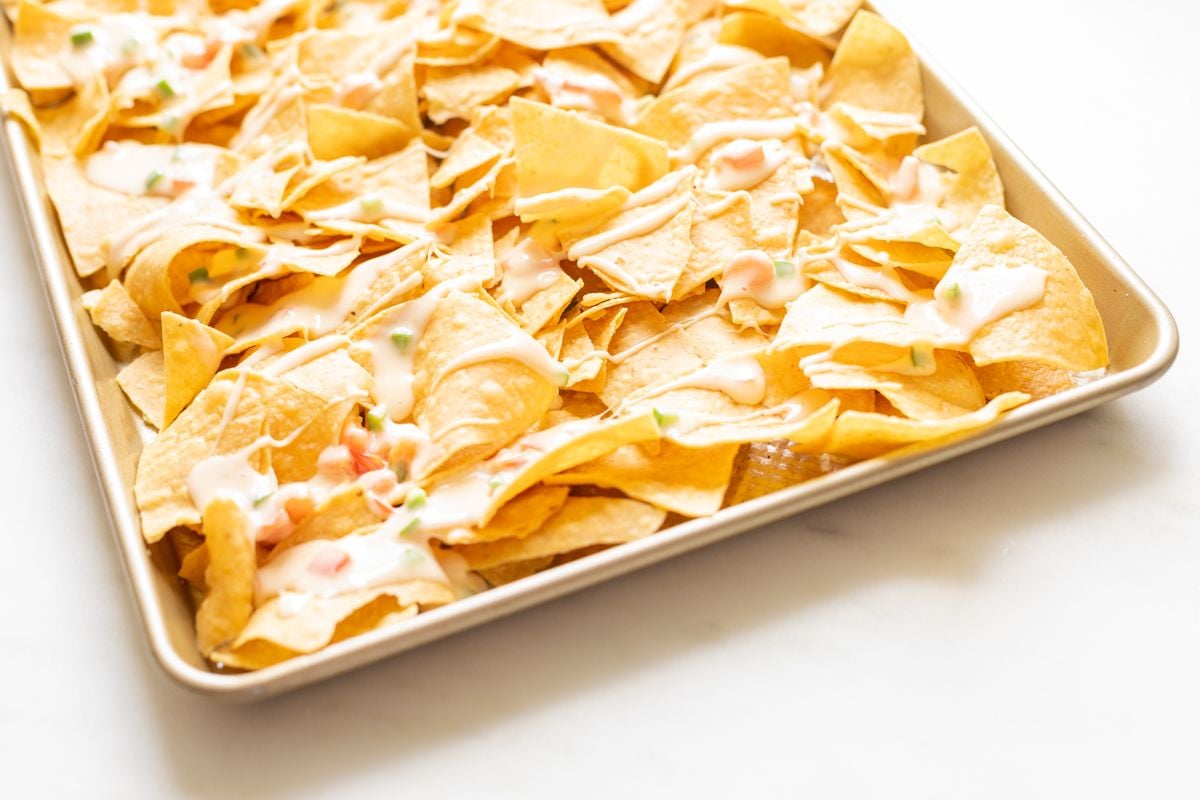 A sheet pan with tortilla chips covered in queso for a chicken nacho recipe.