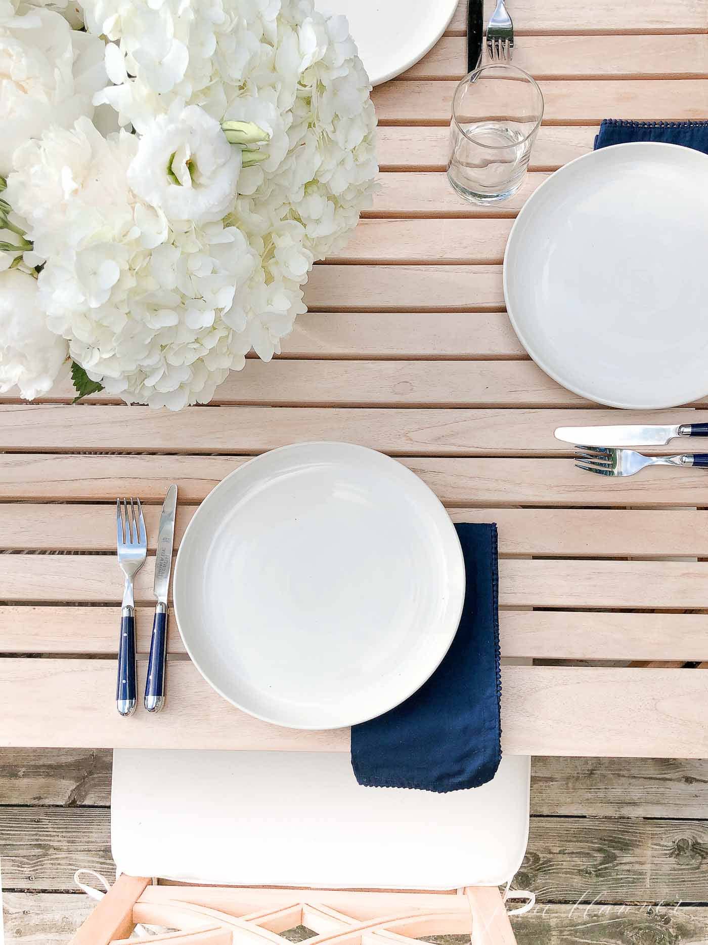 white hydrangea centerpiece on a teak table outdoors.