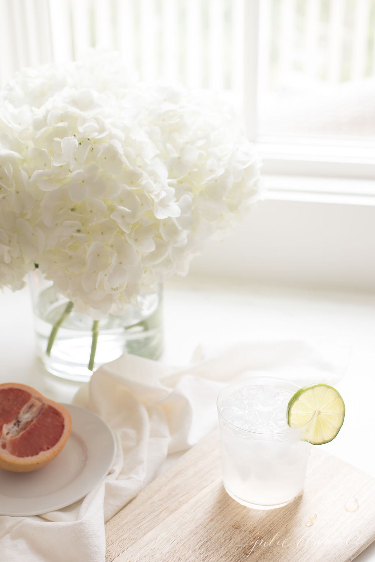 A paloma cocktail in a kitchen with a white flower arrangement in background.