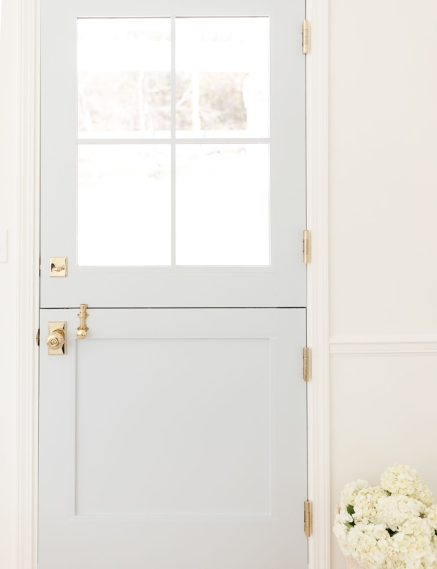 A pale blue dutch door with a basket of white flowers nearby