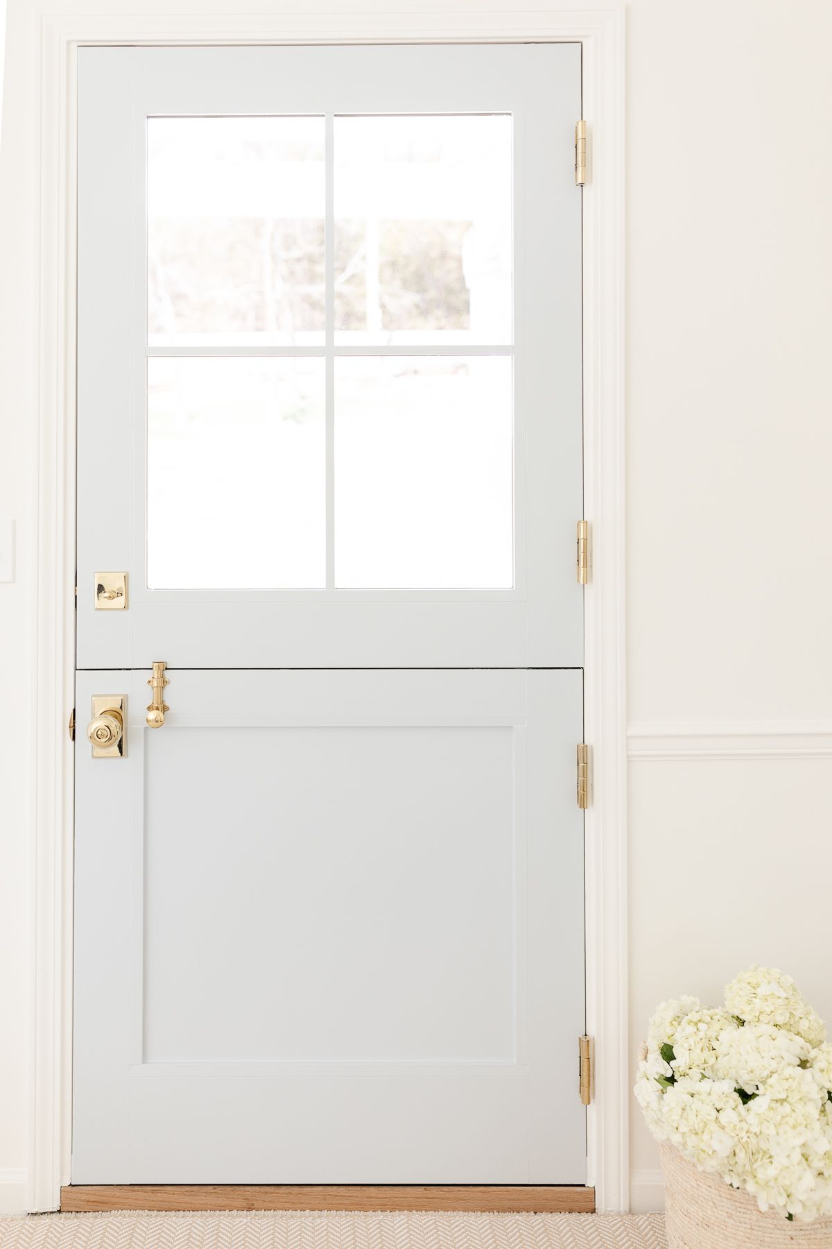 A pale blue dutch door with a basket of white flowers nearby