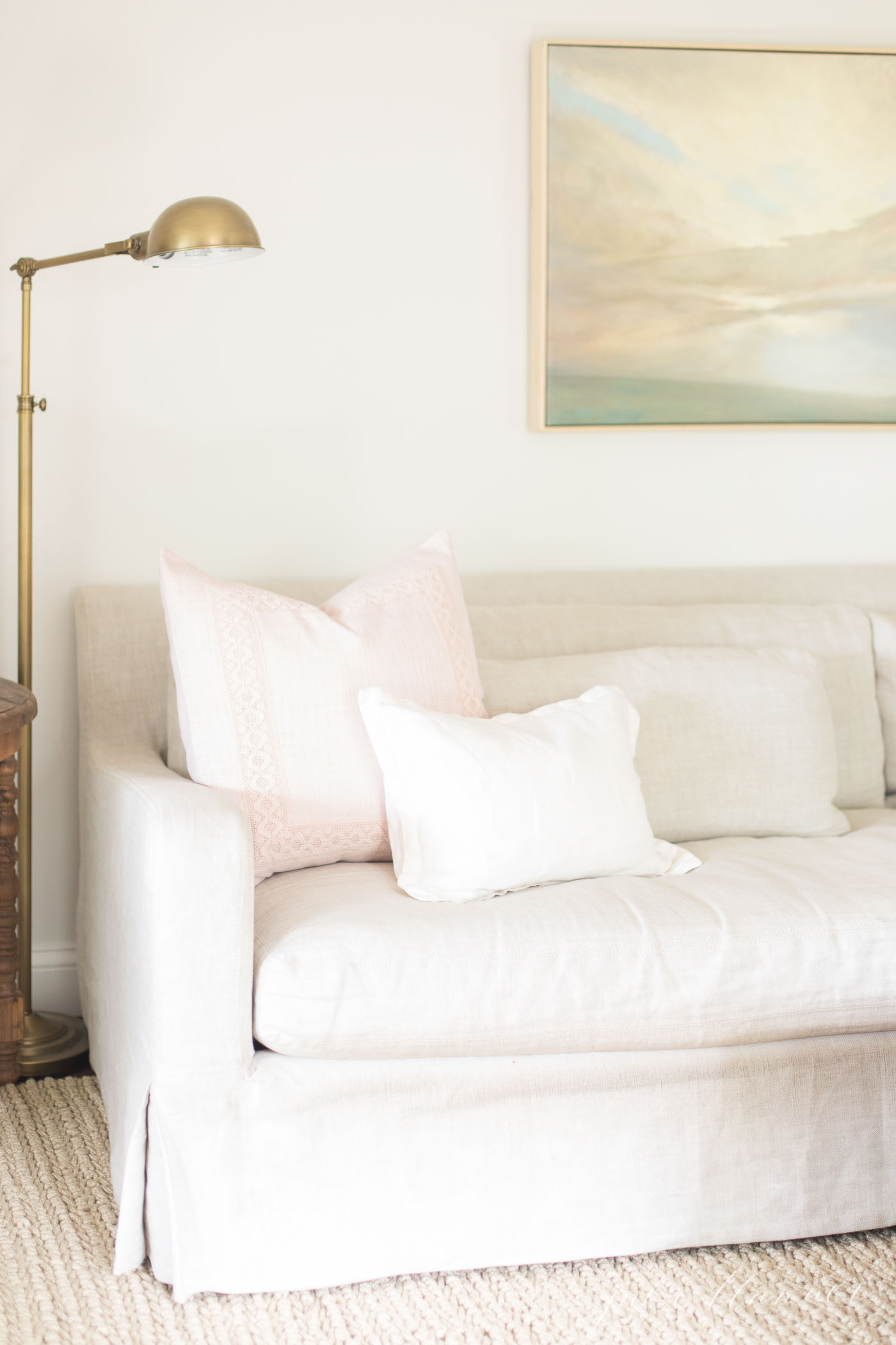 A white living room with a linen sofa placed on a jute look pet friendly rug.