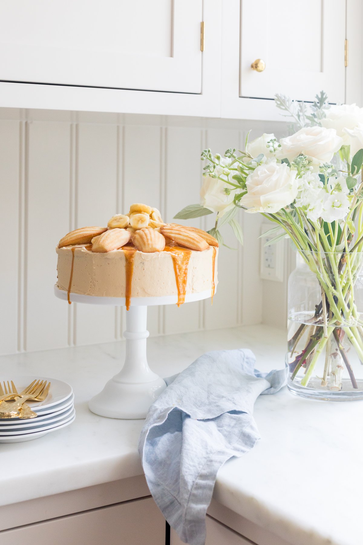 A round banana cake topped with madeleine cookies and caramel sauce. 