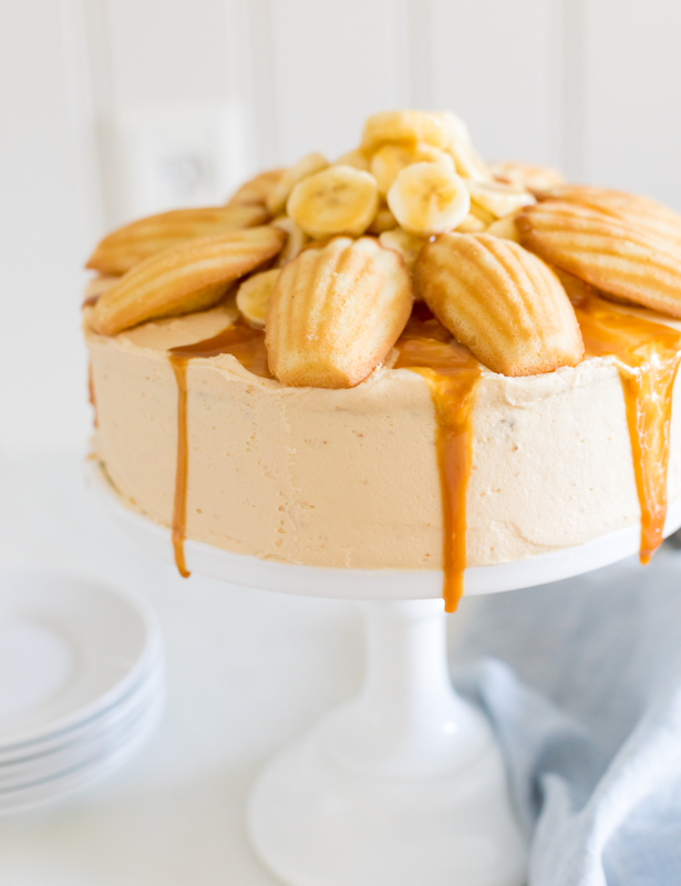 A round banana cake topped with madeleine cookies and caramel sauce.