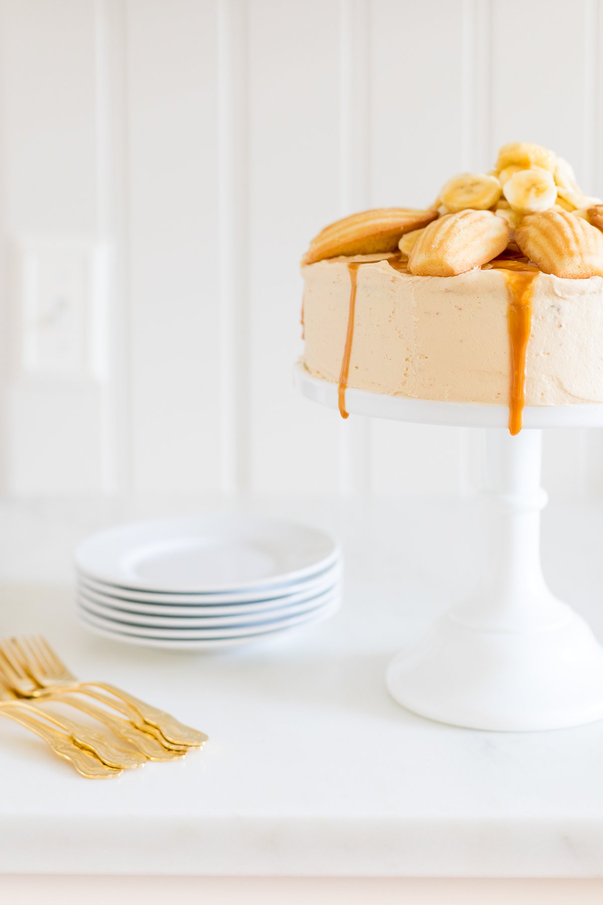 A round banana cake topped with madeleine cookies and caramel sauce.