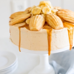 A round banana cake topped with madeleine cookies and caramel sauce.