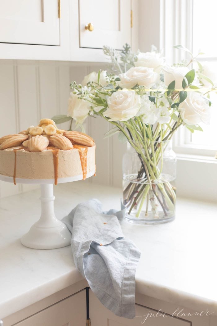 A banana cake on a stand next to flowers