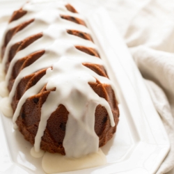 A chocolate chip pound cake covered in glaze on a white platter
