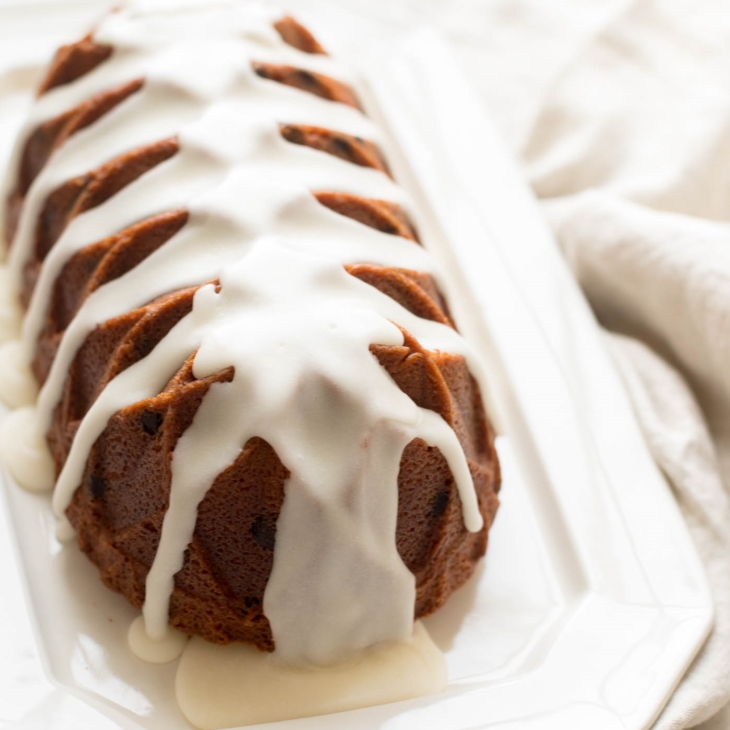 A chocolate chip pound cake covered in glaze on a white platter
