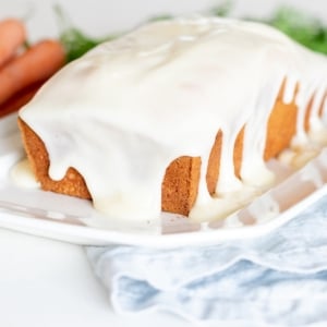 A carrot cake with creamy white cream cheese glaze on a plate.