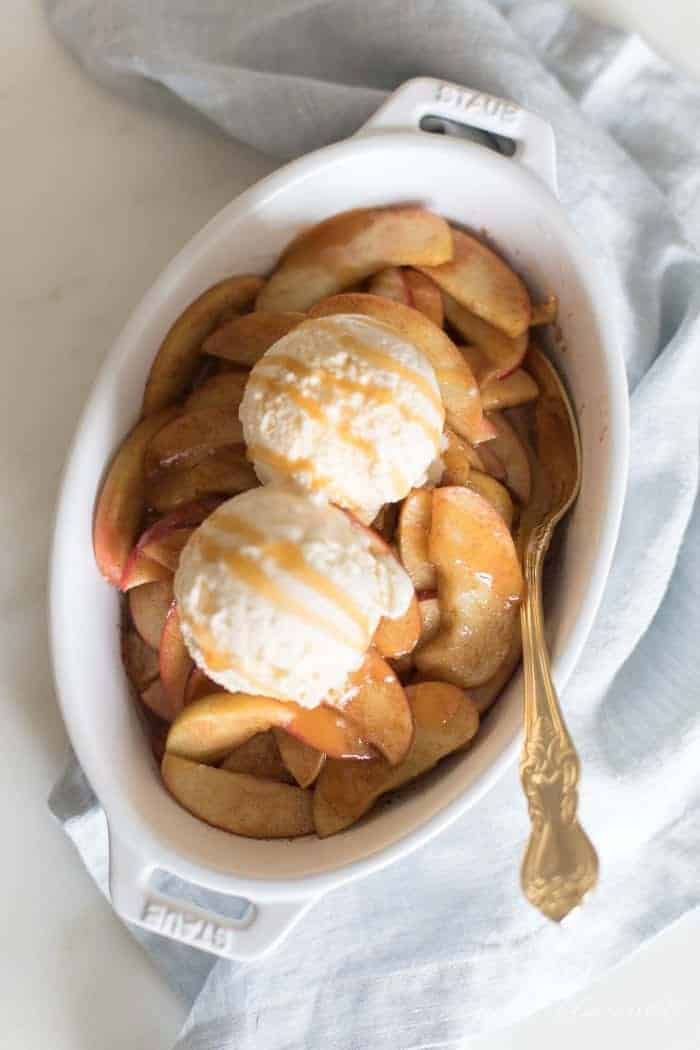 A white oval baking dish filled with baked apple slices, topped with scoops of ice cream.