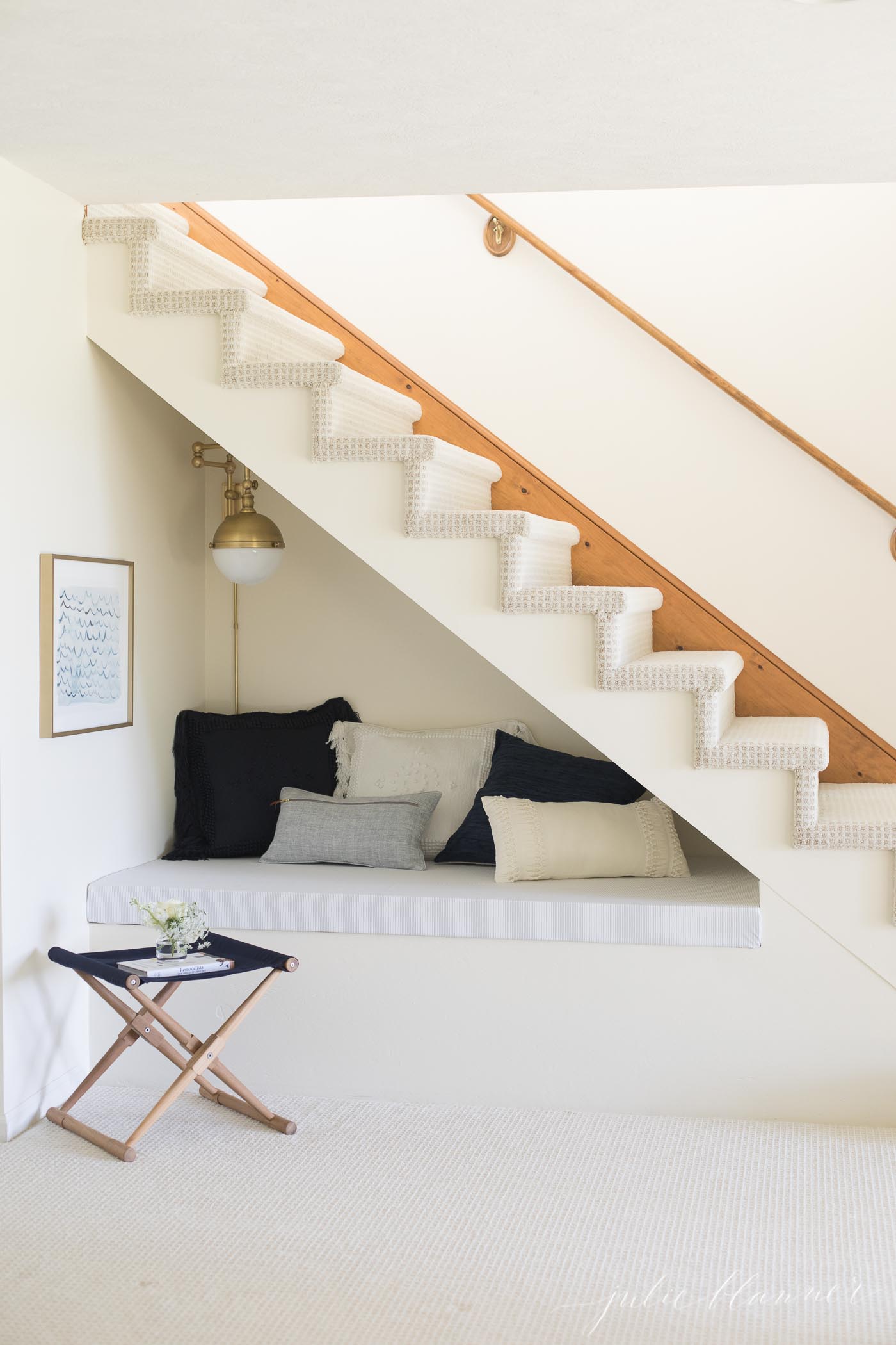 A living room with light carpet and a built in reading nook under stairs
