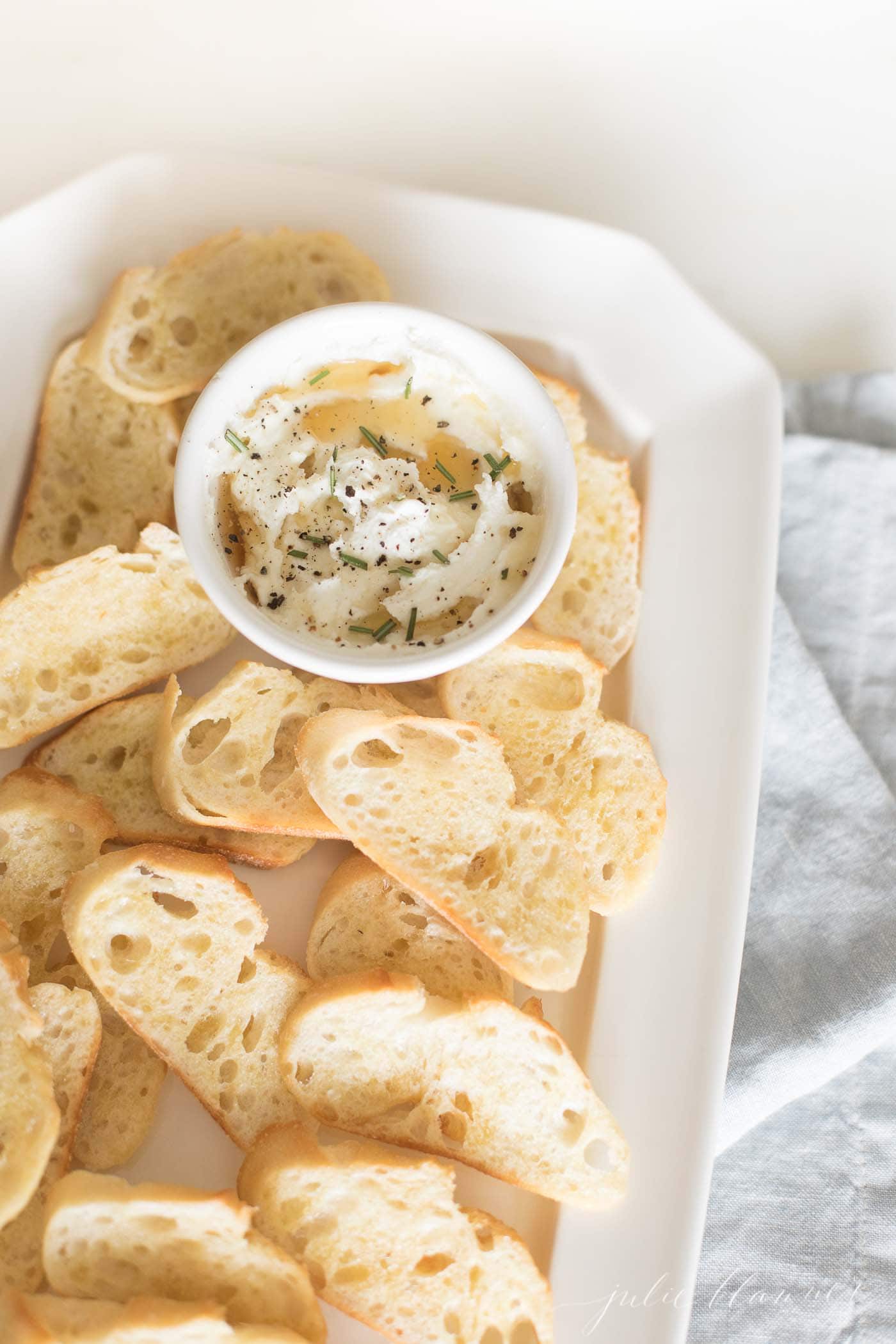 honey whipped goat cheese in a white bowl surrounded by sliced crostini.