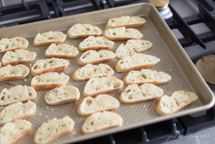 Crostini slices on a sheet pan on top of a stovetop. 