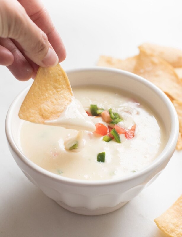 tortilla chip dipped in queso blanco dip in a white bowl