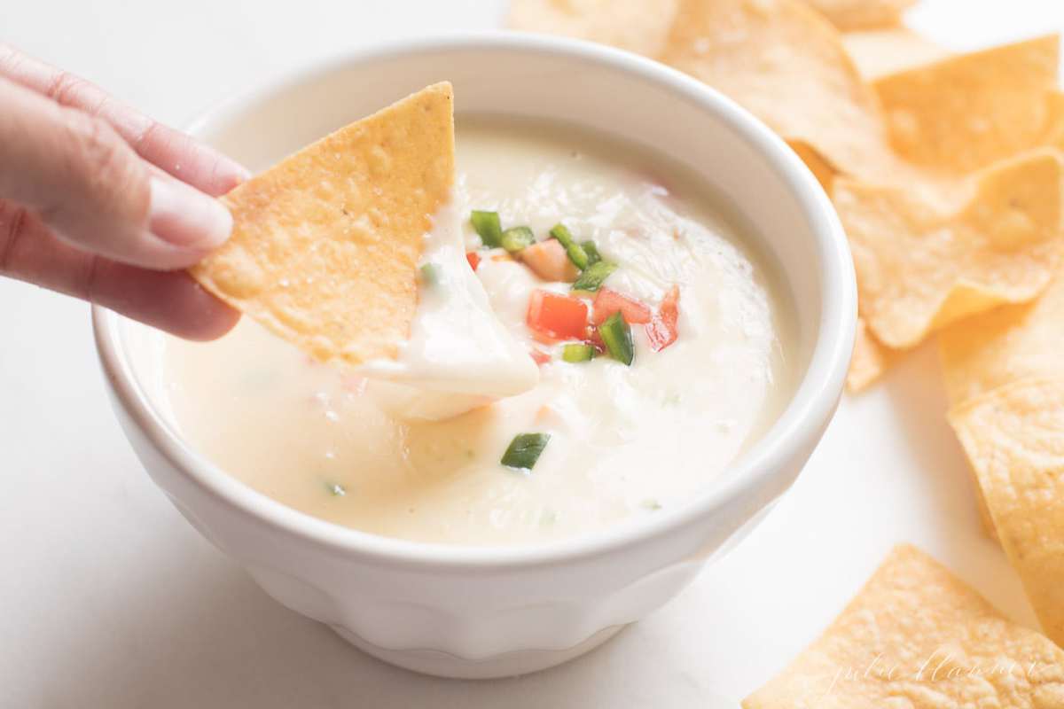 tortilla chip dipped in queso blanco dip in a white bowl