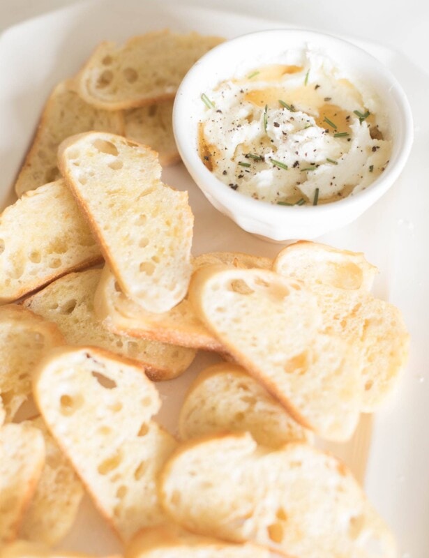 whipped goat cheese with honey on a white platter of crostini