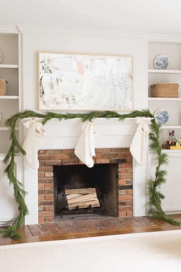 A brick fireplace decorated with Christmas greens, with a custom sisal rug with border on the floor of a home living room.