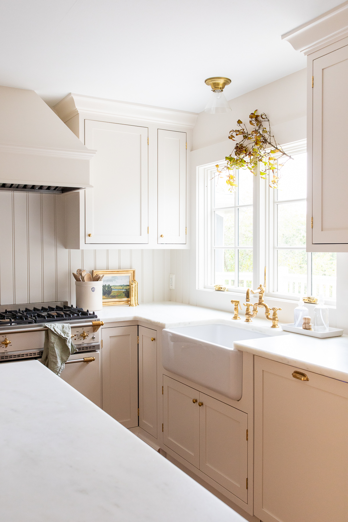 A kitchen with white cabinets and a white sink, with a fall branch hanging above