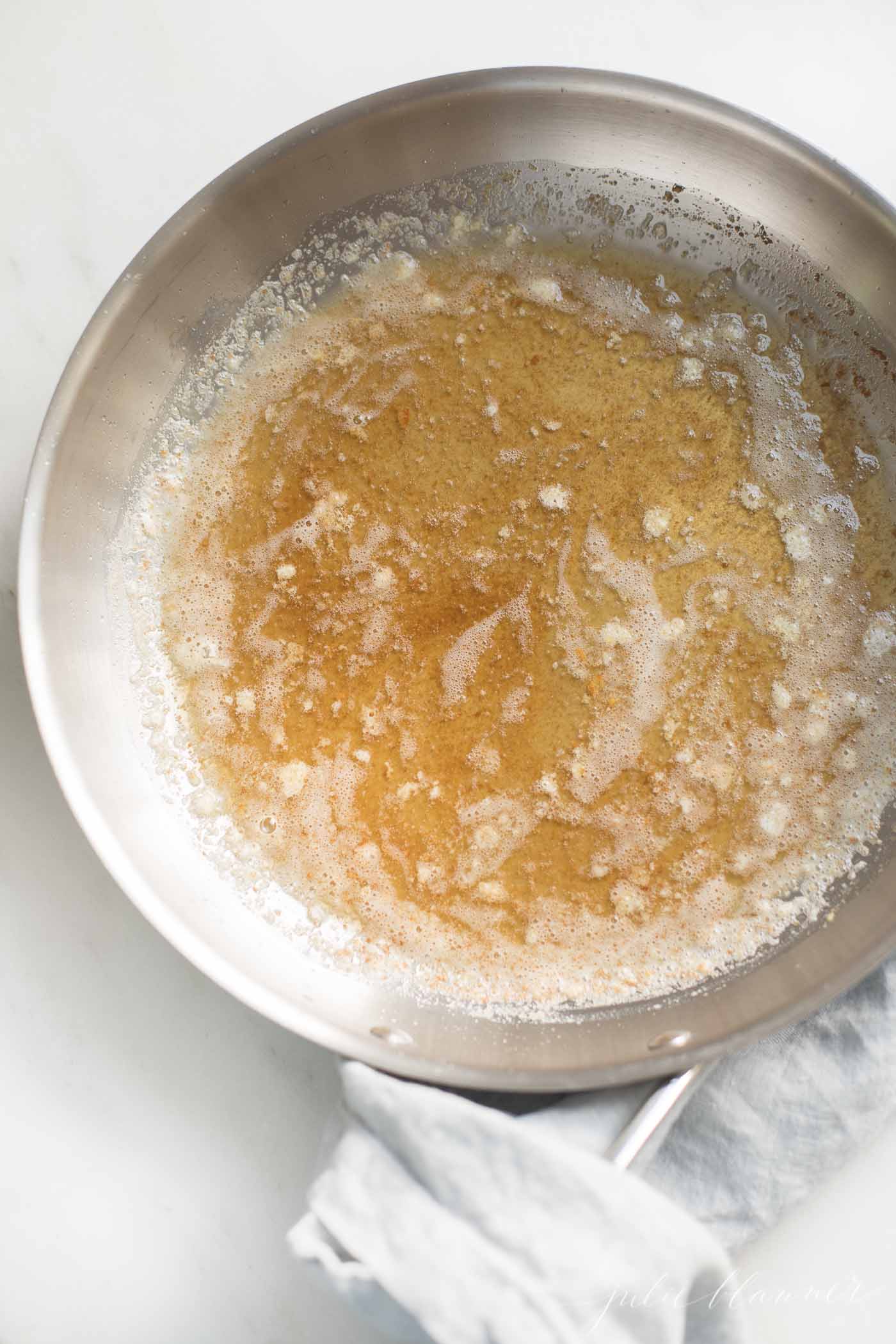 A silver pan with handle, warm browned butter inside, showing how to brown butter.