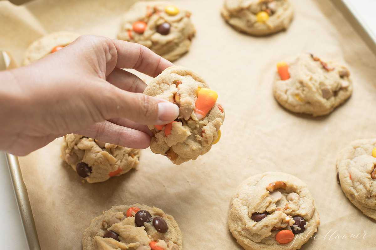 Monster Cookies on a baking sheet with a hand holding one cookie.