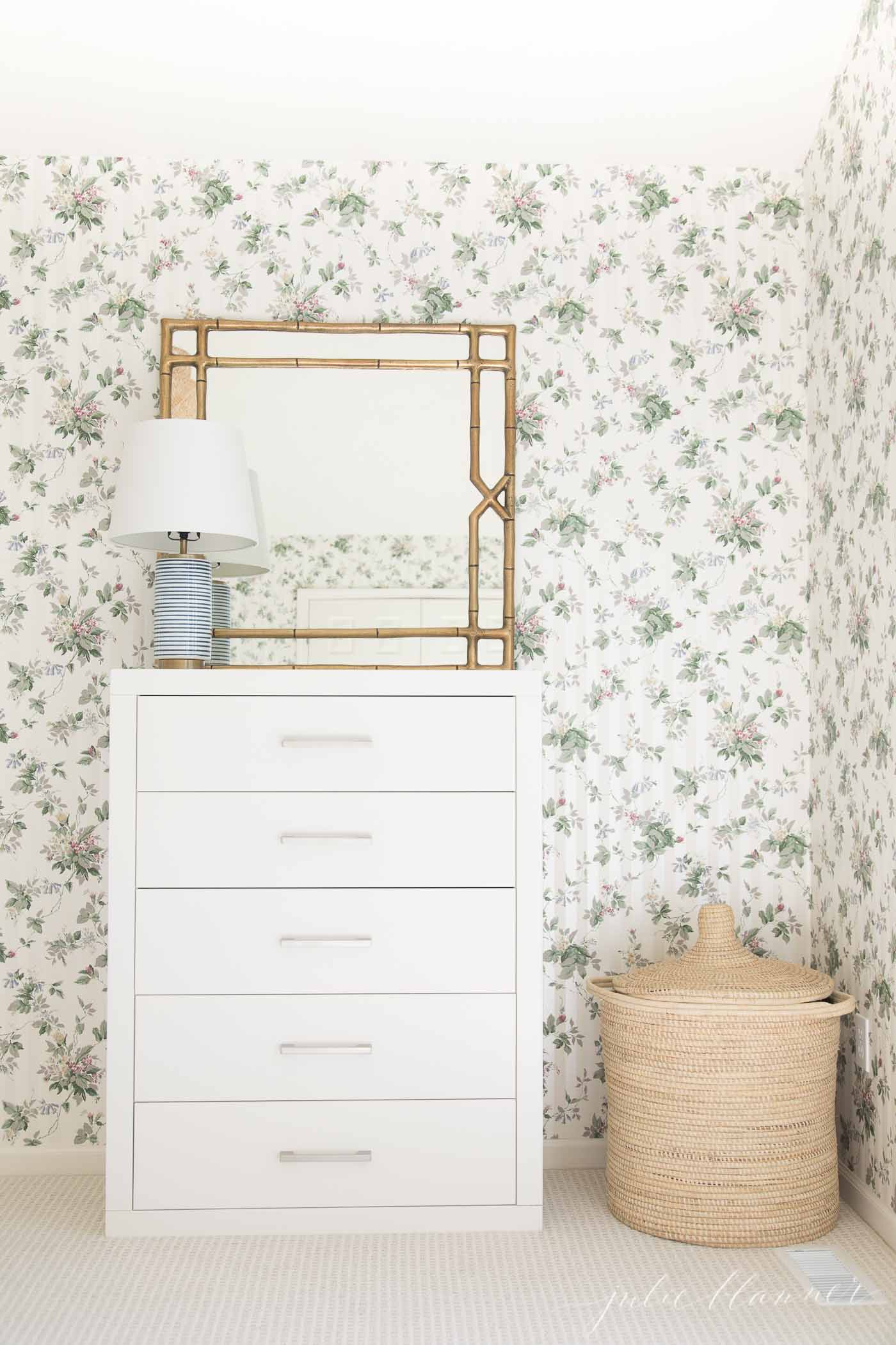 A white dresser in a bedroom with floral wallpaper and beige patterned carpet.