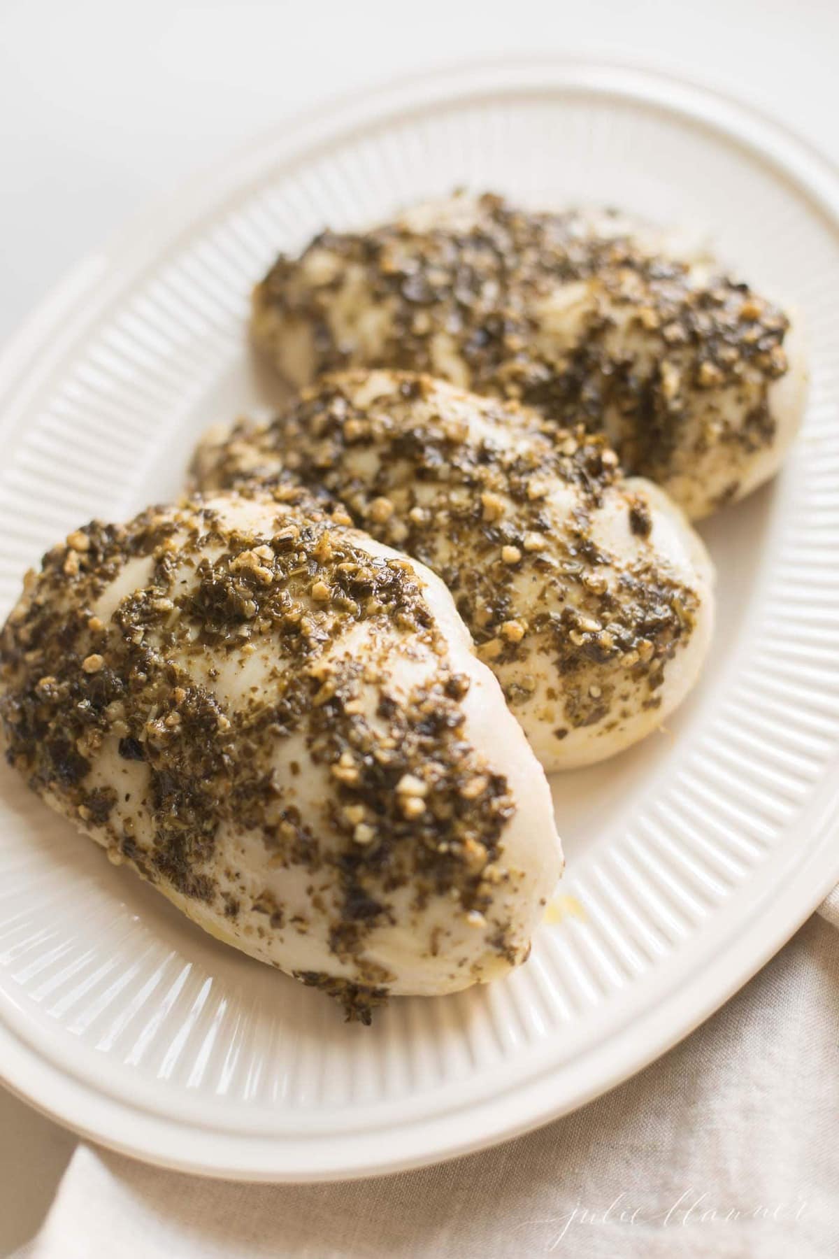 A white platter with three pesto baked chicken breasts.