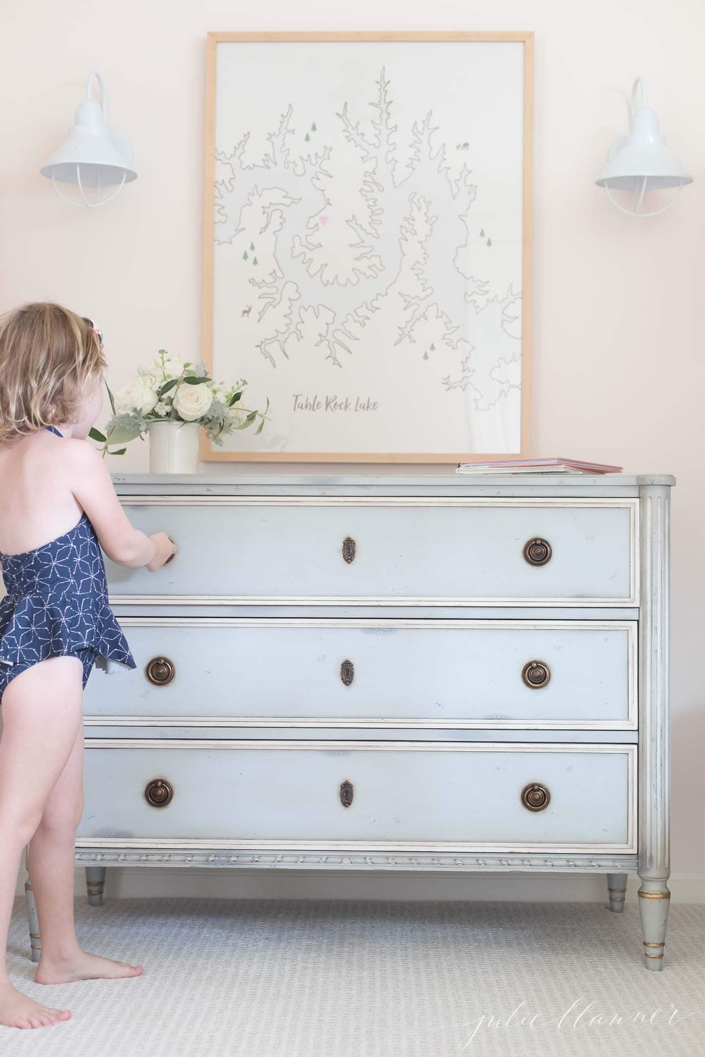 patterned carpet and a soft blue dresser in a little girl's bedroom, girl in swimsuit opening the dresser.