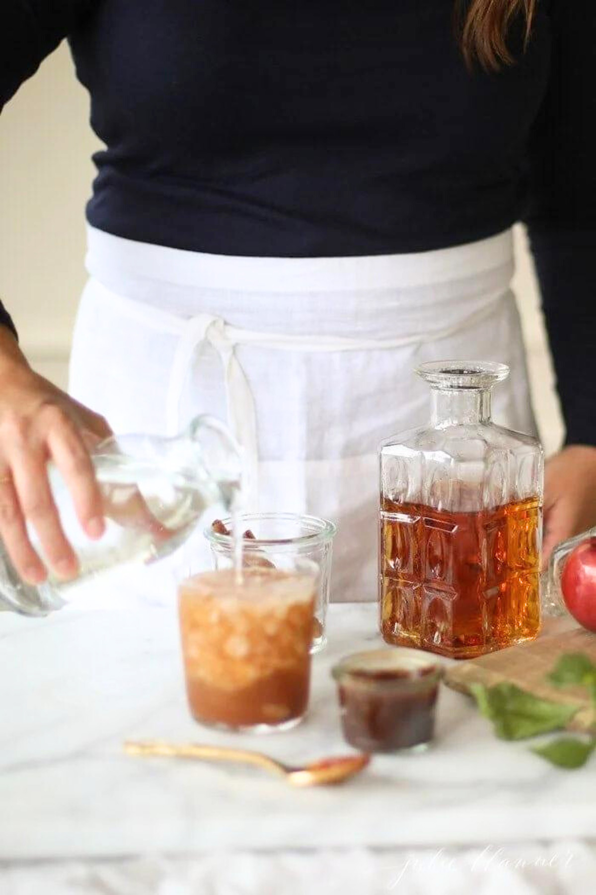 A woman wearing a black shirt, creating an apple butter old fashioned at a bar.