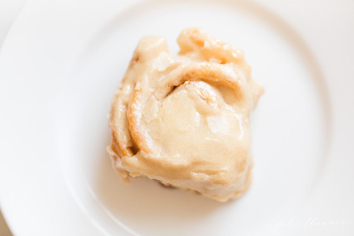 Soft, moist, Caramel Rolls topped with Caramel Frosting - so good you'd never know this Caramel Rolls Recipe starts from a can of crescent sheets! A frosted roll on a white plate
