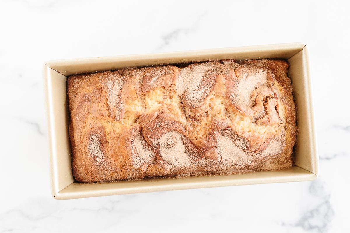 Cinnamon roll bread baked in a gold loaf pan on a marble surface