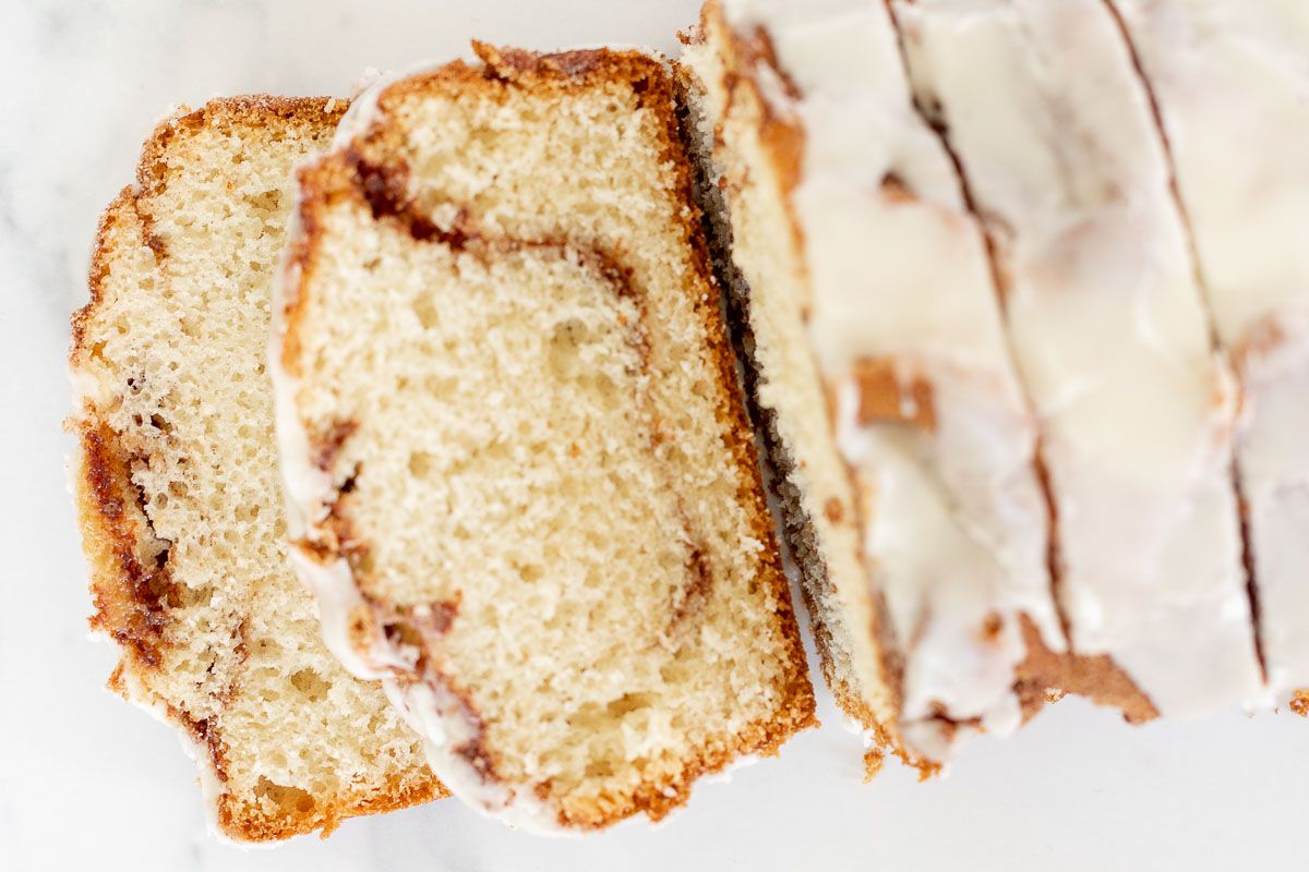 A loaf of cinnamon roll bread, covered in icing and sliced on a marble surface