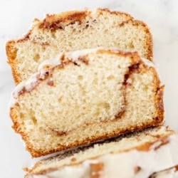 A loaf of cinnamon roll bread, covered in icing and sliced on a marble surface