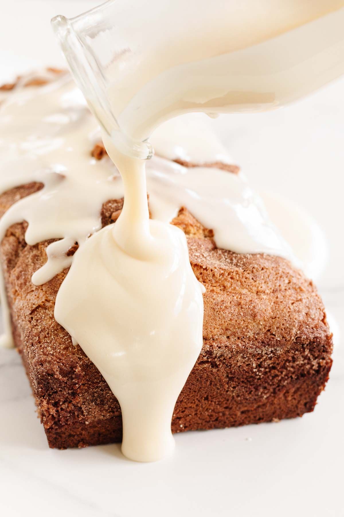 Creamy icing pouring over a loaf of cinnamon roll bread