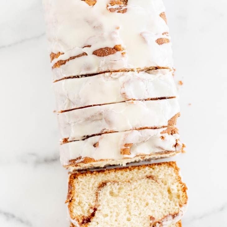 A loaf of cinnamon roll bread, covered in icing and sliced on a marble surface