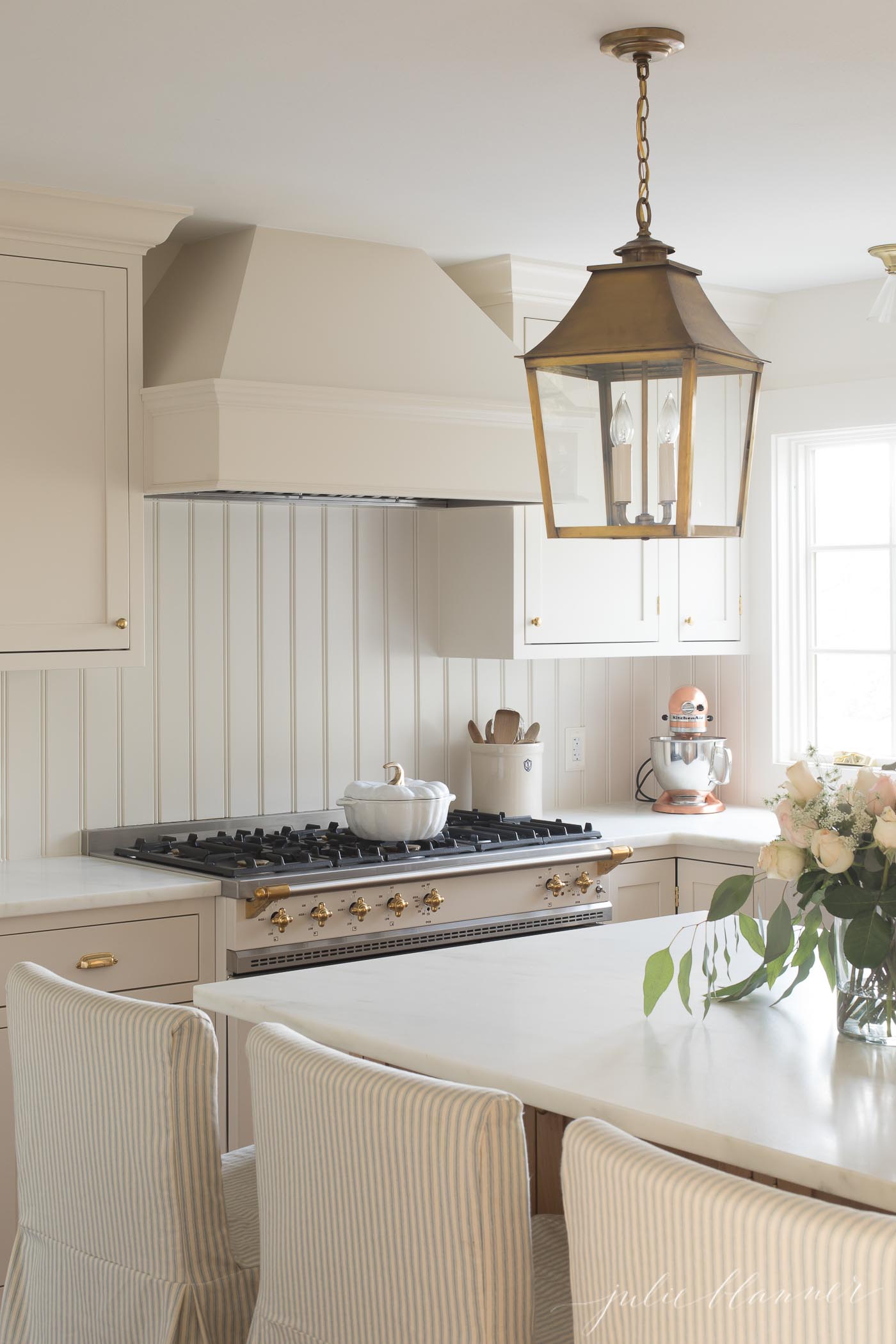 slipcovered barstools in a cream colored kitchen with a brass lantern above island