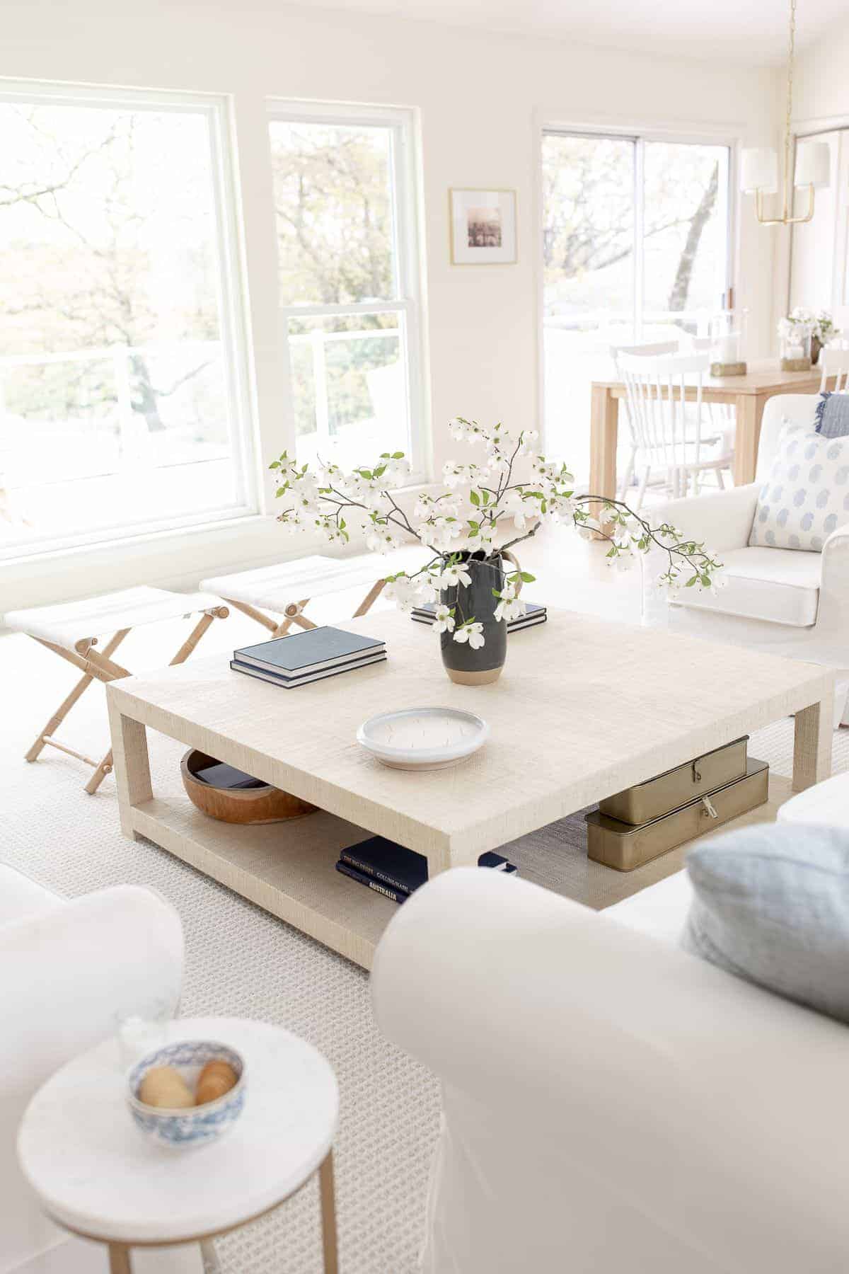 A raffia coffee table decorated in a coastal living room, with a navy vase of blooming branches.