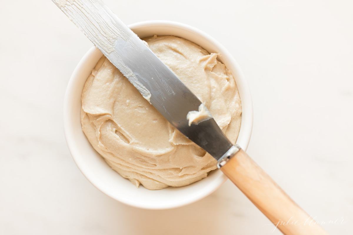 caramel icing in a small white bowl, spreading knife rests on top.