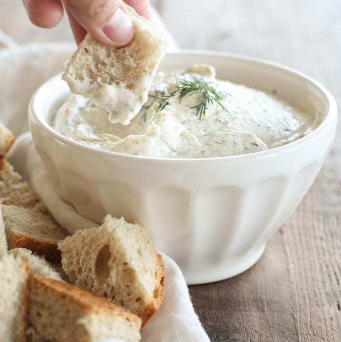 hand dipping into bowl of dill dip with rye bread