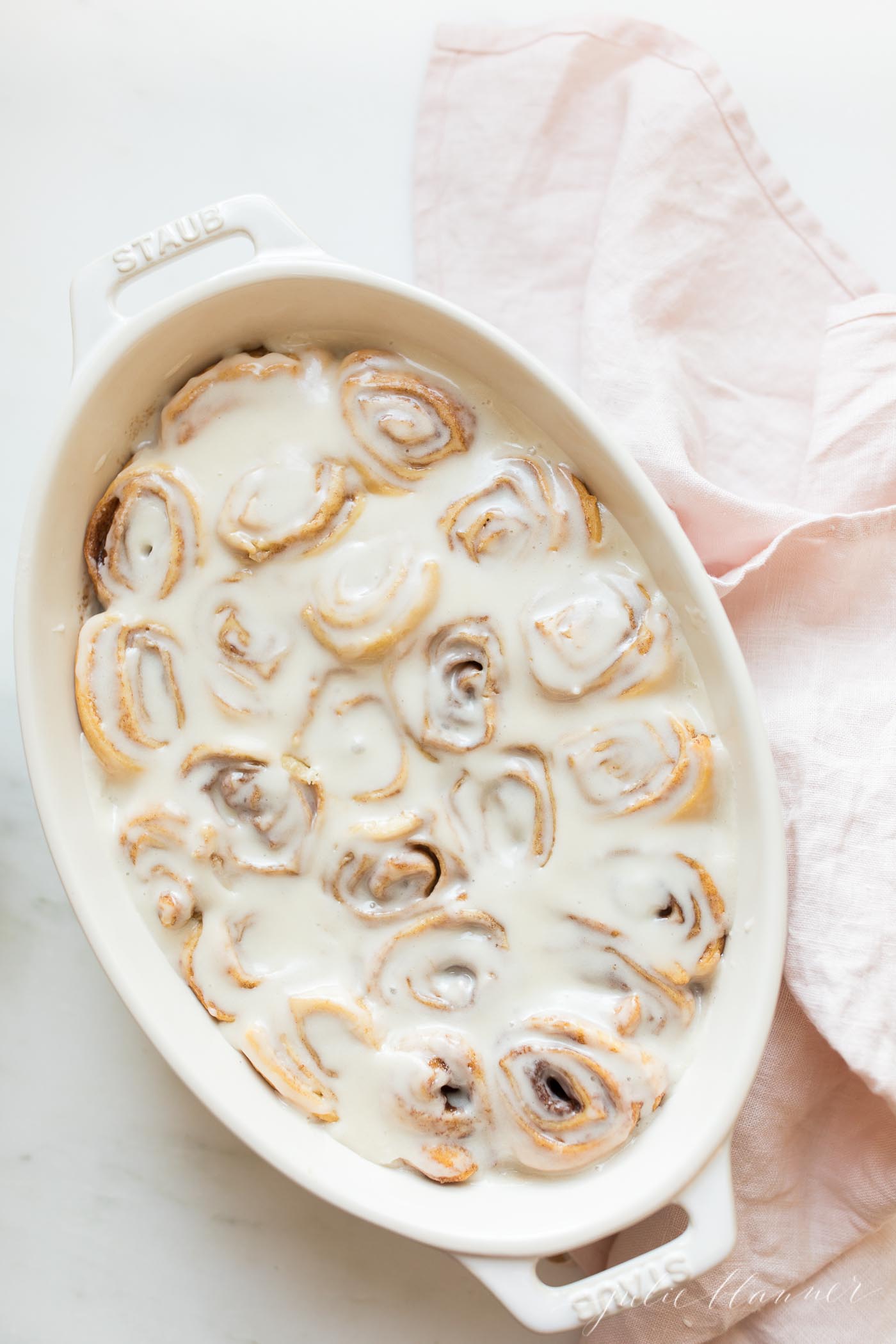 cinnamon rolls in cream baking dish covered in icing