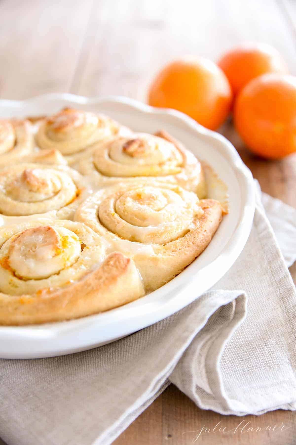 A white pan full of homemade orange rolls, whole oranges in the background.