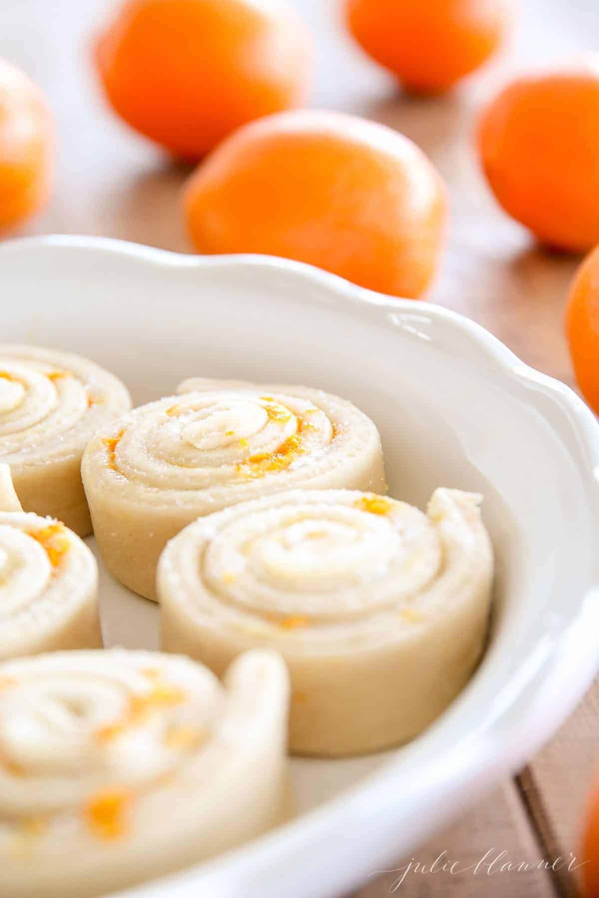 A white pan full of uncooked homemade orange roll recipe, whole oranges in the background.