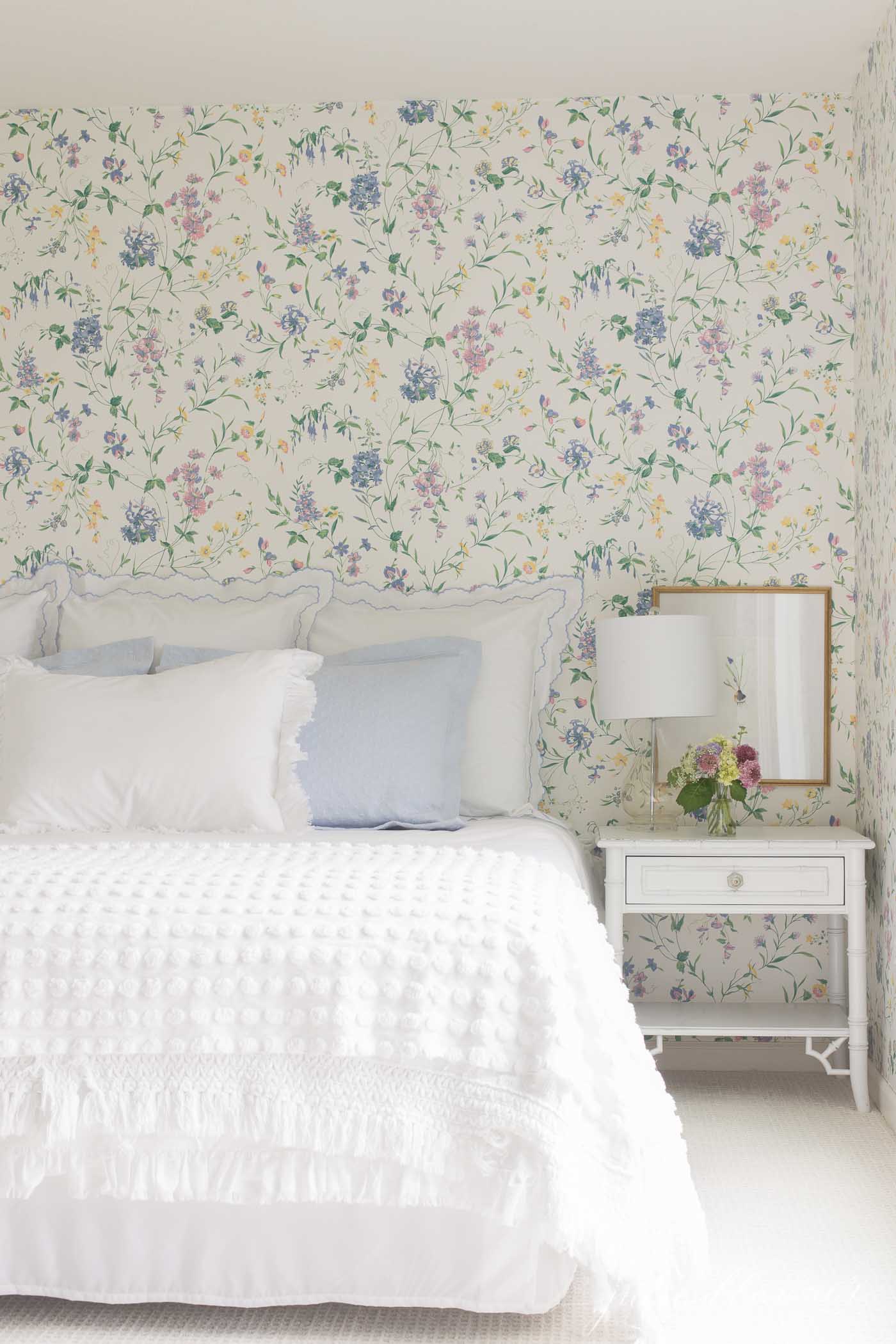 A floral wallpapered guest bedroom with blue and white bedding.