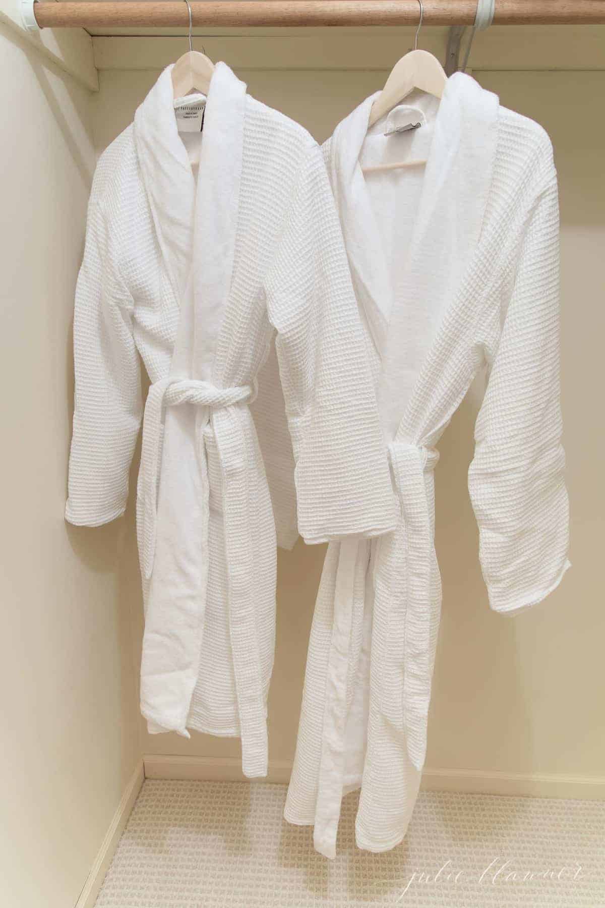 Two white bath robes hanging in a guest room closet.
