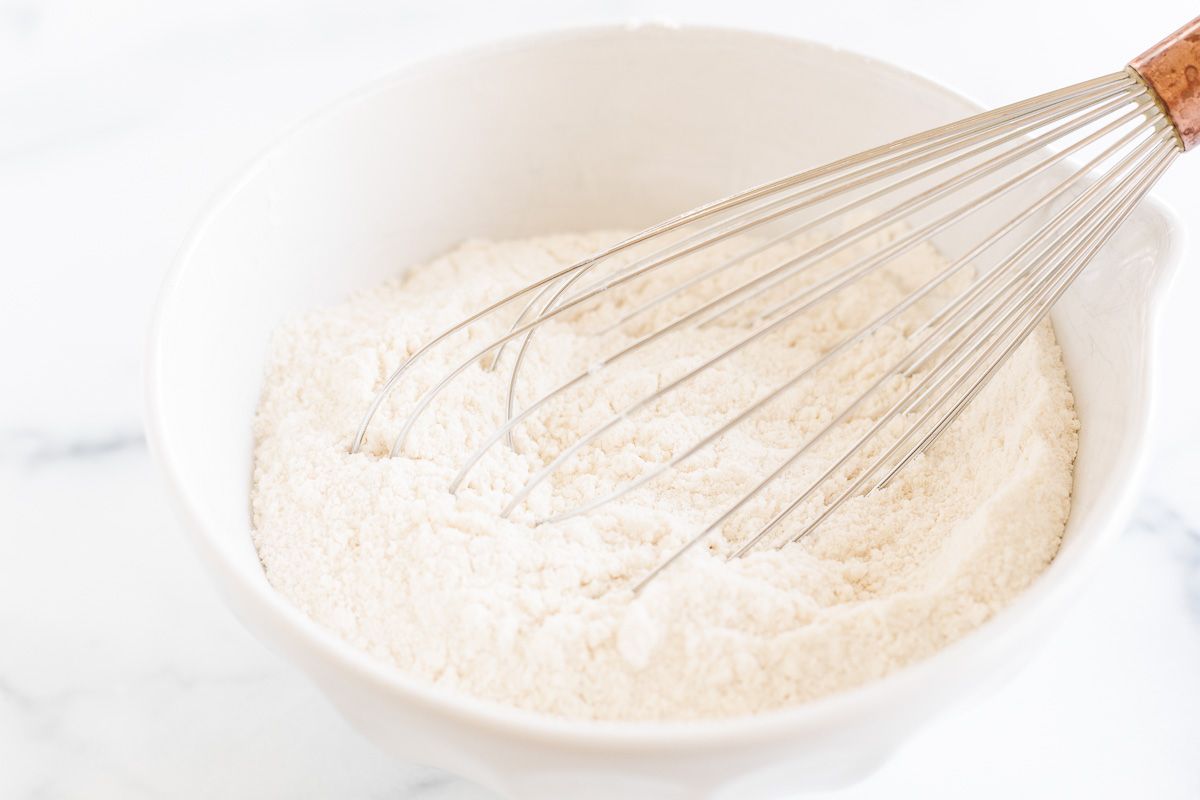A mixture of flour in a white bowl with a large metal whisk