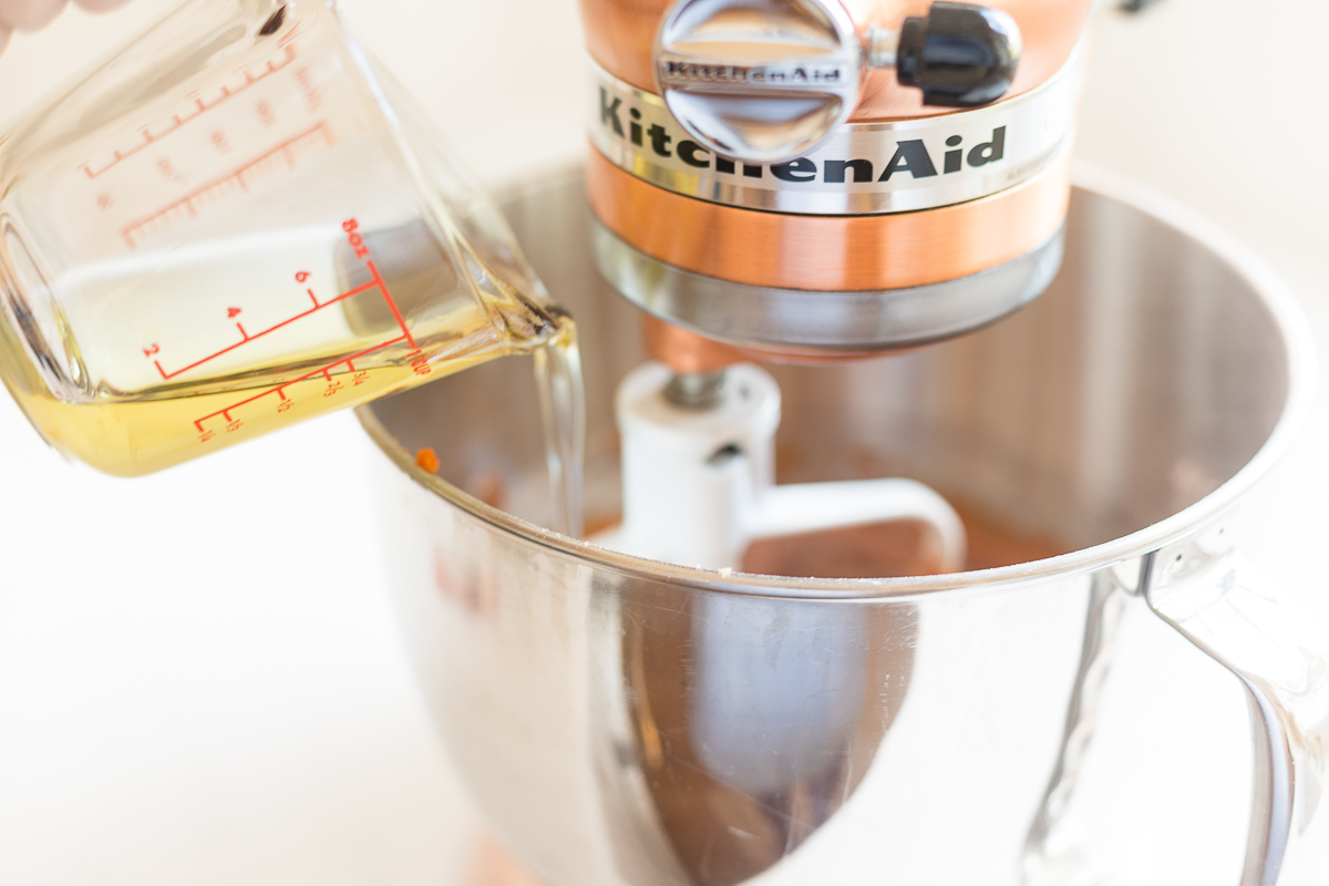 A measuring cup pouring oil into a stand mixer bowl.