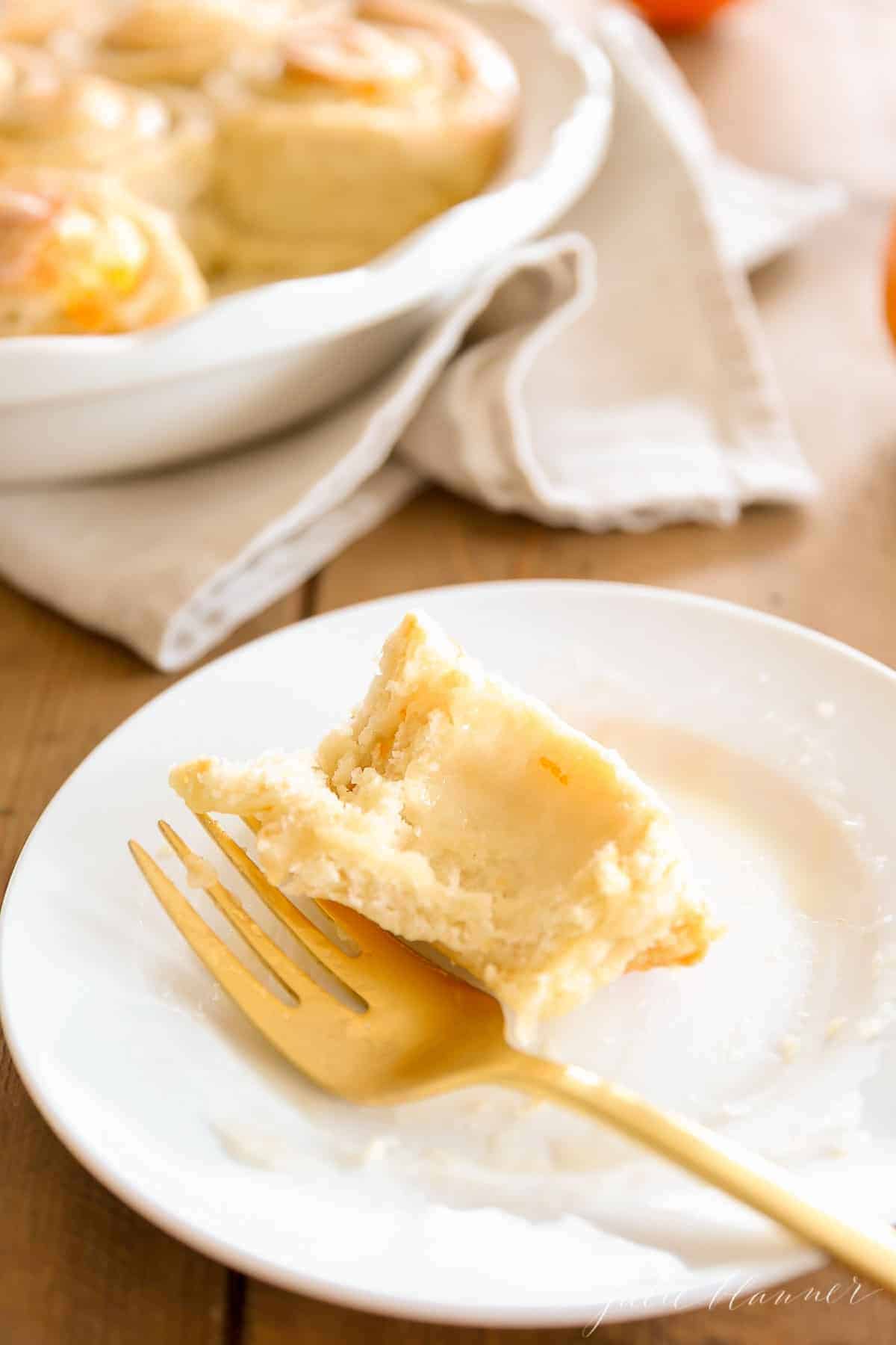 A piece of a homemade orange roll on a white plate with a gold fork.